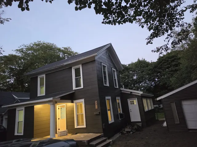 Two-story home painted dark gray with white trim and a lit front porch at dusk